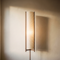 Washi-style paper floor lamp, lit, on a plaster backdrop